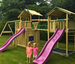 Houten speeltoestel met twee glijbanen, klimnet, netbrug en schommels in een tuin